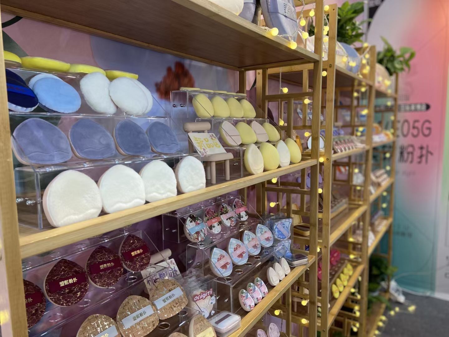 Display of colorful beauty sponges and powder puffs on wooden shelves with decorative lights.