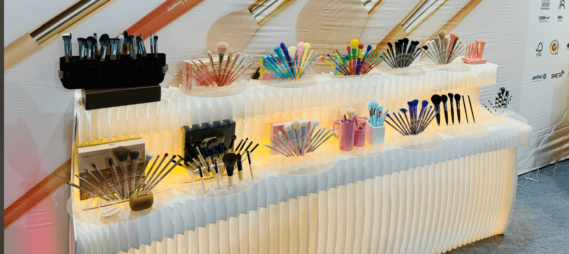 Display of various colorful makeup brushes arranged on tiered shelves against a decorative backdrop.